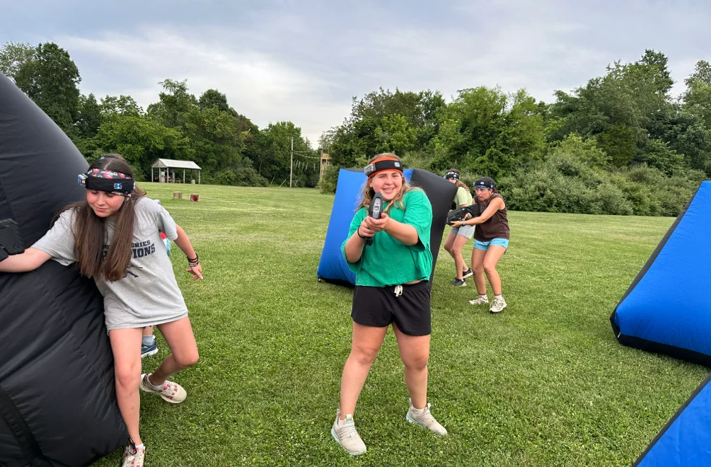 Camper aiming a laser tag blaster during an outdoor summer camp mission