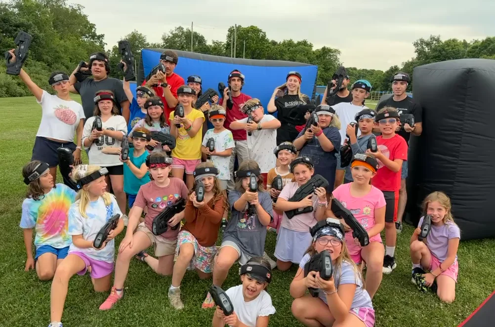 Group of campers posing with laser tag blasters at an outdoor summer camp event
