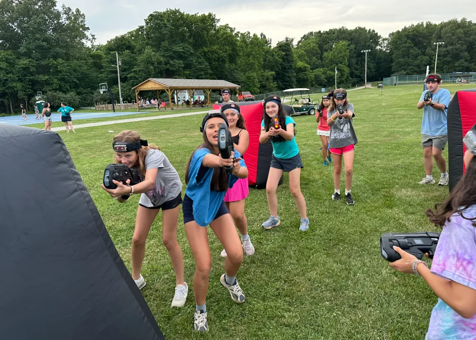 Campers lined up taking aim during an outdoor laser tag battle at summer camp