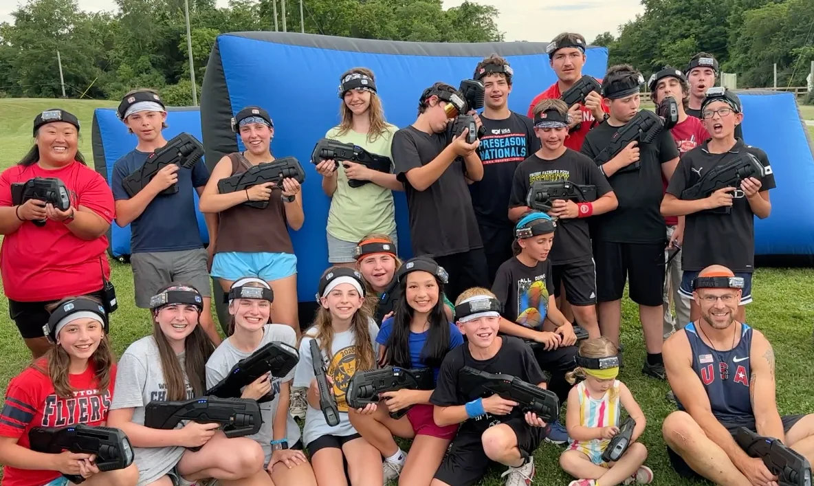 Teen camp group posing with laser tag blasters on an outdoor field