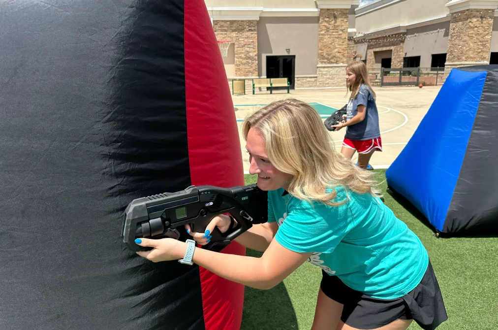 Camp counselor aiming a laser tag blaster from behind a bunker