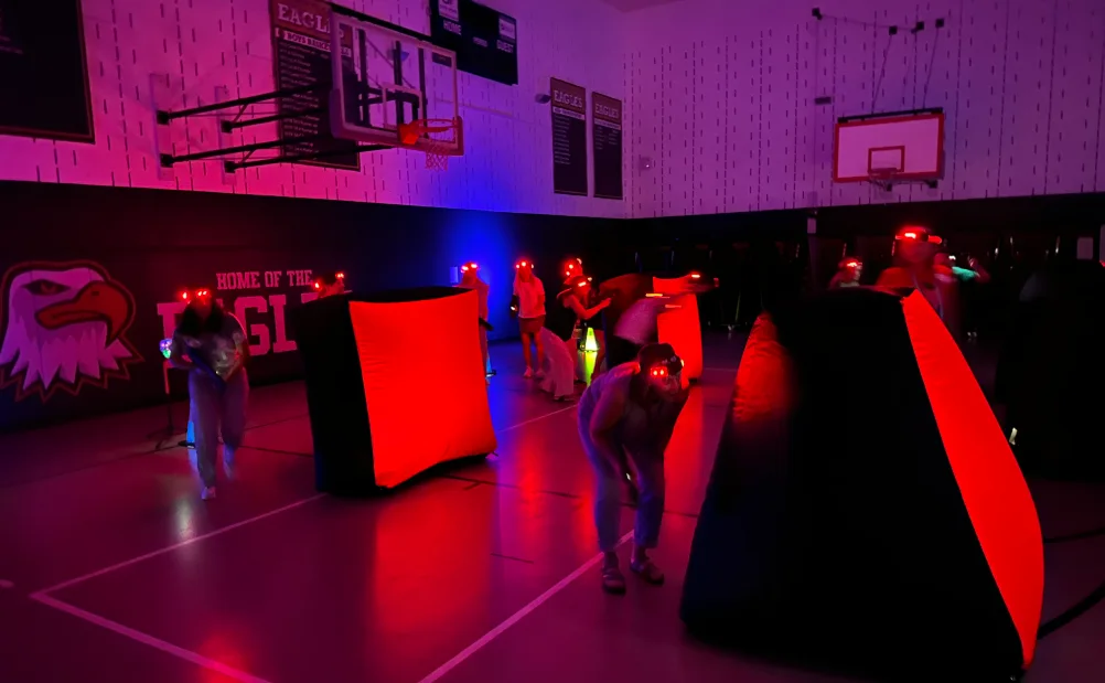 Players with headlamps taking cover behind bunkers in a school gym decorated with its team mascot