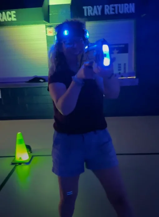 Player aiming a laser tag blaster in a school hallway during a community glow event