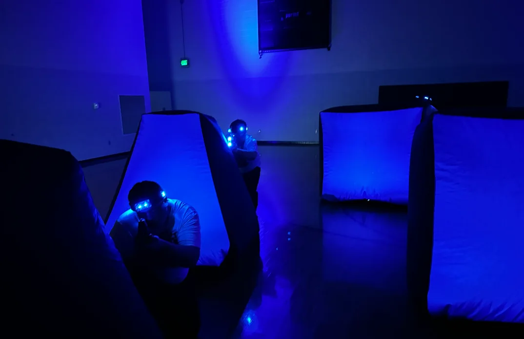 Two students taking cover behind glowing blue bunkers during an After Prom laser tag match