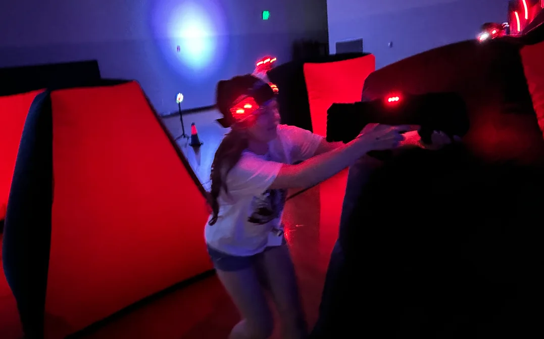 Student taking aim from behind a red-lit bunker during an After Prom laser tag match