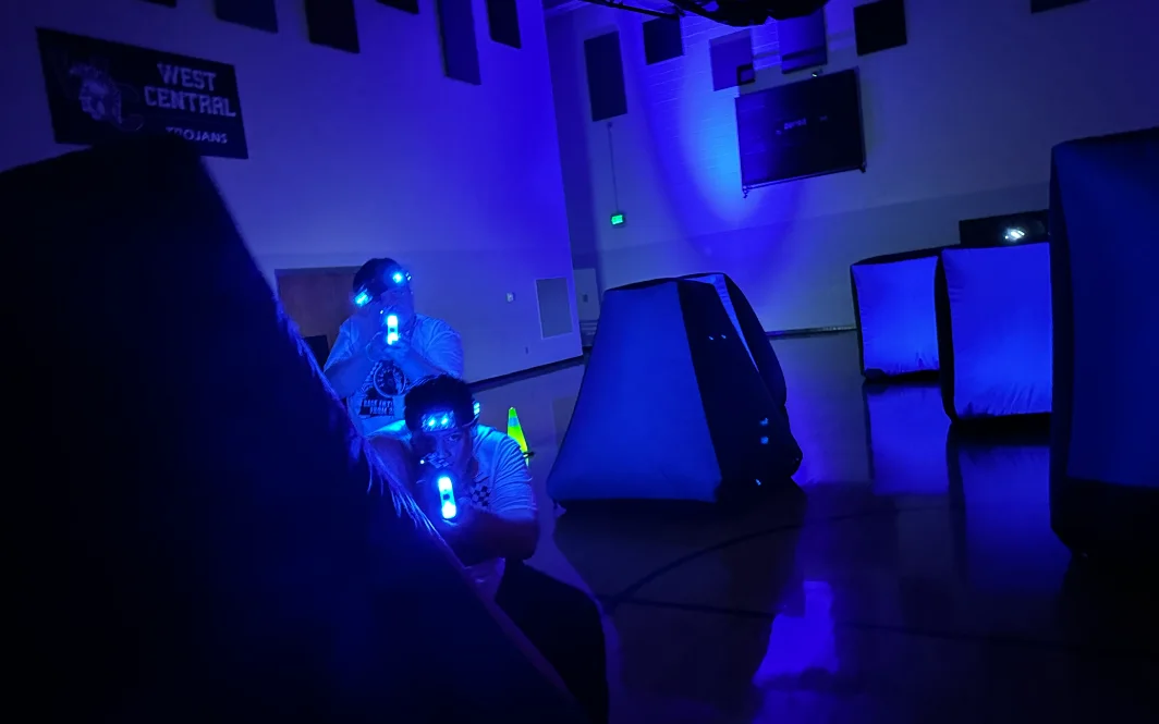 Two students crouched behind an inflatable bunker taking aim during an After Prom laser tag mission