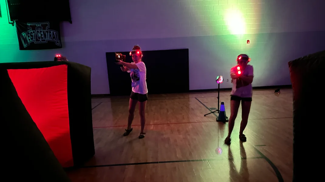 Students aiming laser tag blasters in a green and red lit gymnasium during a school After Prom event