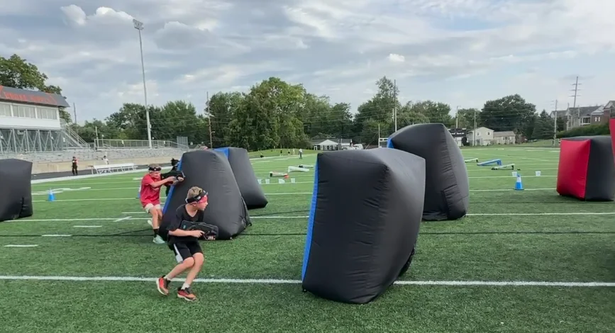 Students running between inflatable bunkers on the football turf during a Broad Ripple Middle School laser tag event