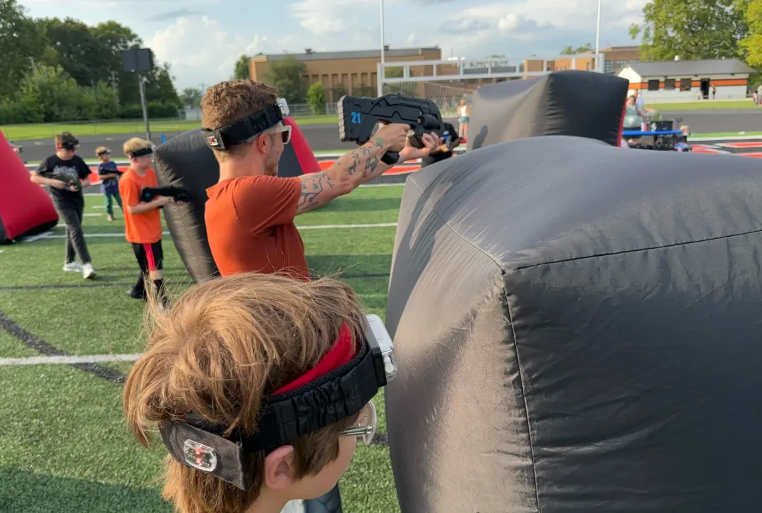 Student and volunteer taking aim from behind a bunker on the turf field at Broad Ripple Middle School