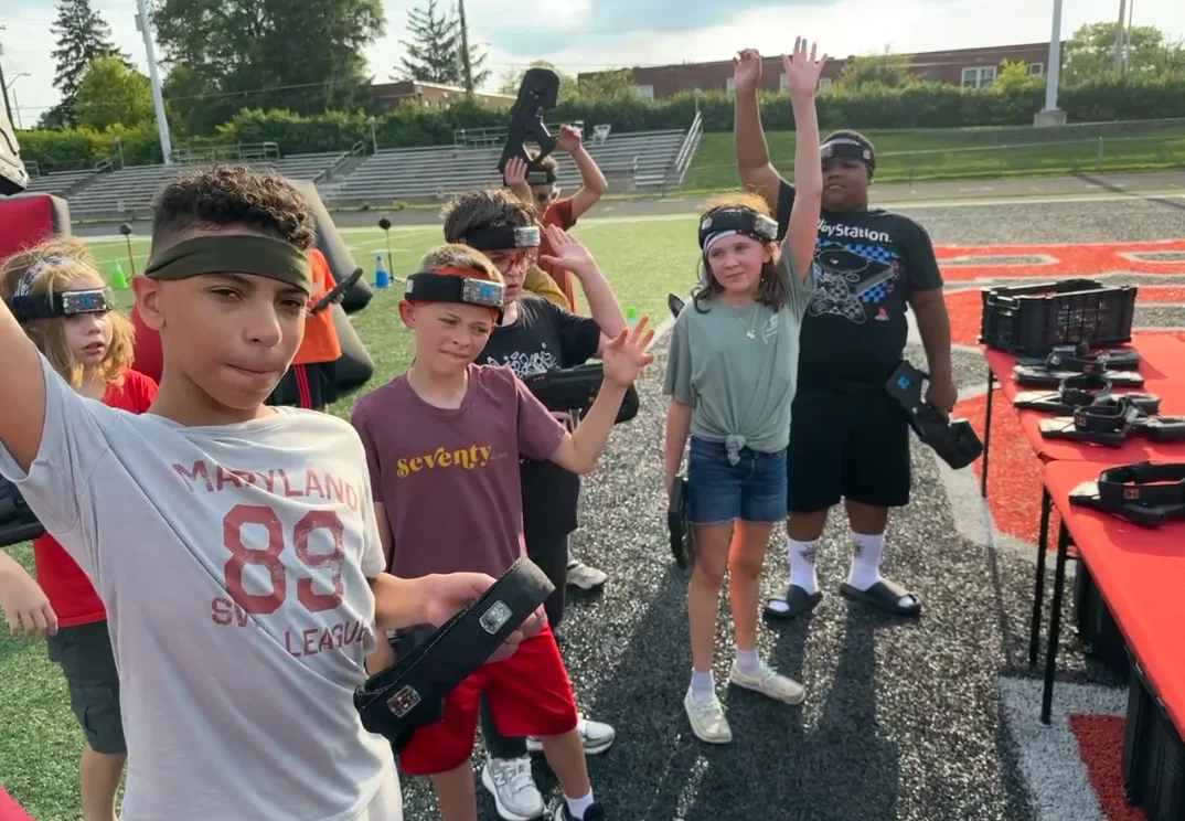 Students cheering with hands raised on the football field bleachers during a Broad Ripple Middle School laser tag event