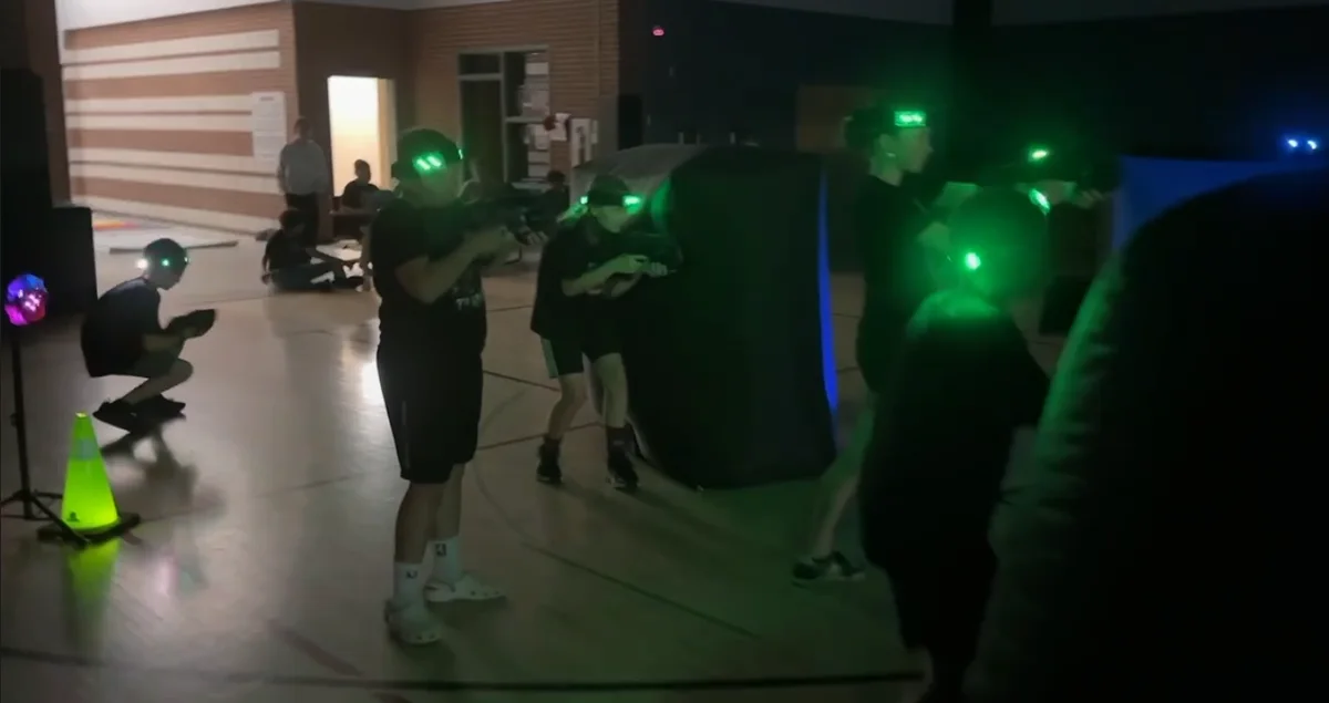 Elementary school students with green headlamps taking cover behind a bunker during a laser tag glow event