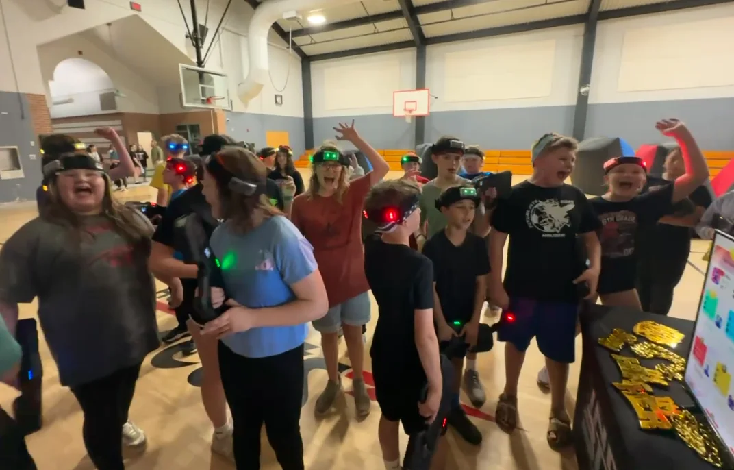 Elementary school students cheering with gold trophies after a daytime laser tag glow event
