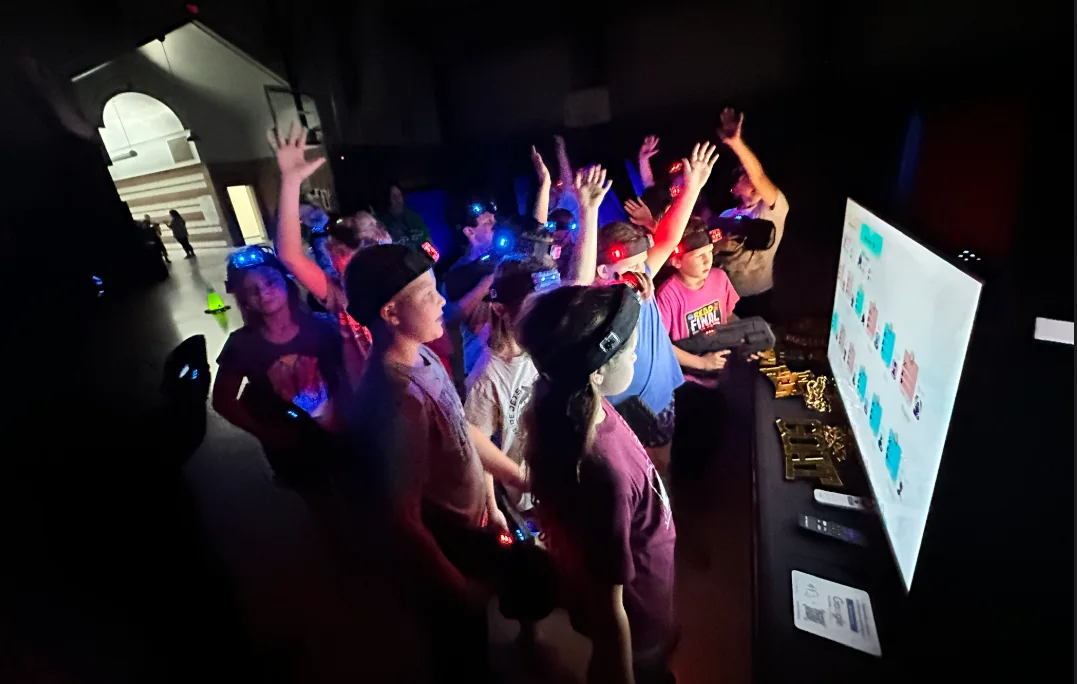 Elementary school students raising their hands and cheering in front of the scoreboard during a laser tag glow event
