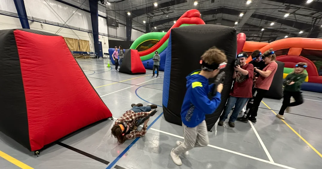 Students taking cover and firing taggers during a middle school laser tag fundraiser