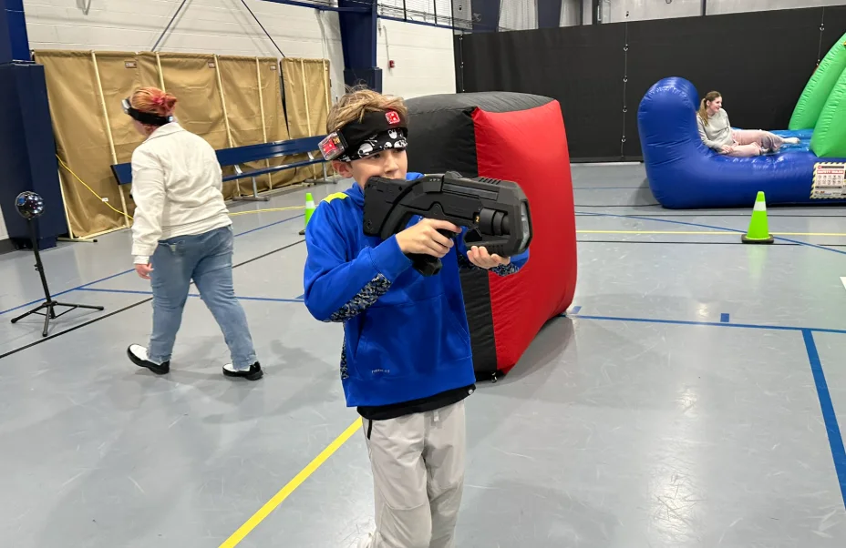 A student aiming a laser tag blaster during a middle school PTO fundraiser night