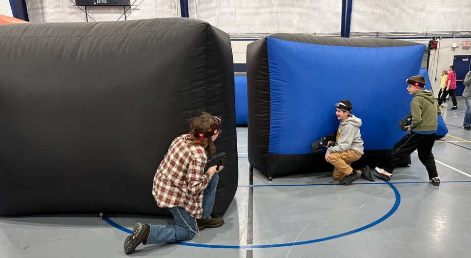 Three students crouched behind bunkers working together during a middle school laser tag fundraiser