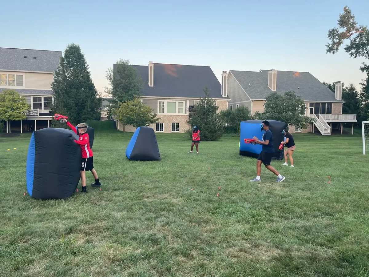 Kids playing Nerf behind inflatable bunkers at an outdoor birthday party