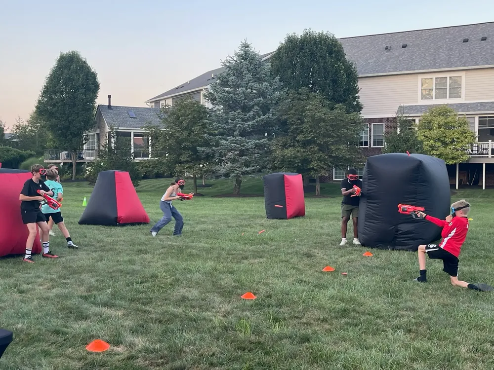 Kids in safety goggles taking cover behind inflatable bunkers during a Nerf birthday party